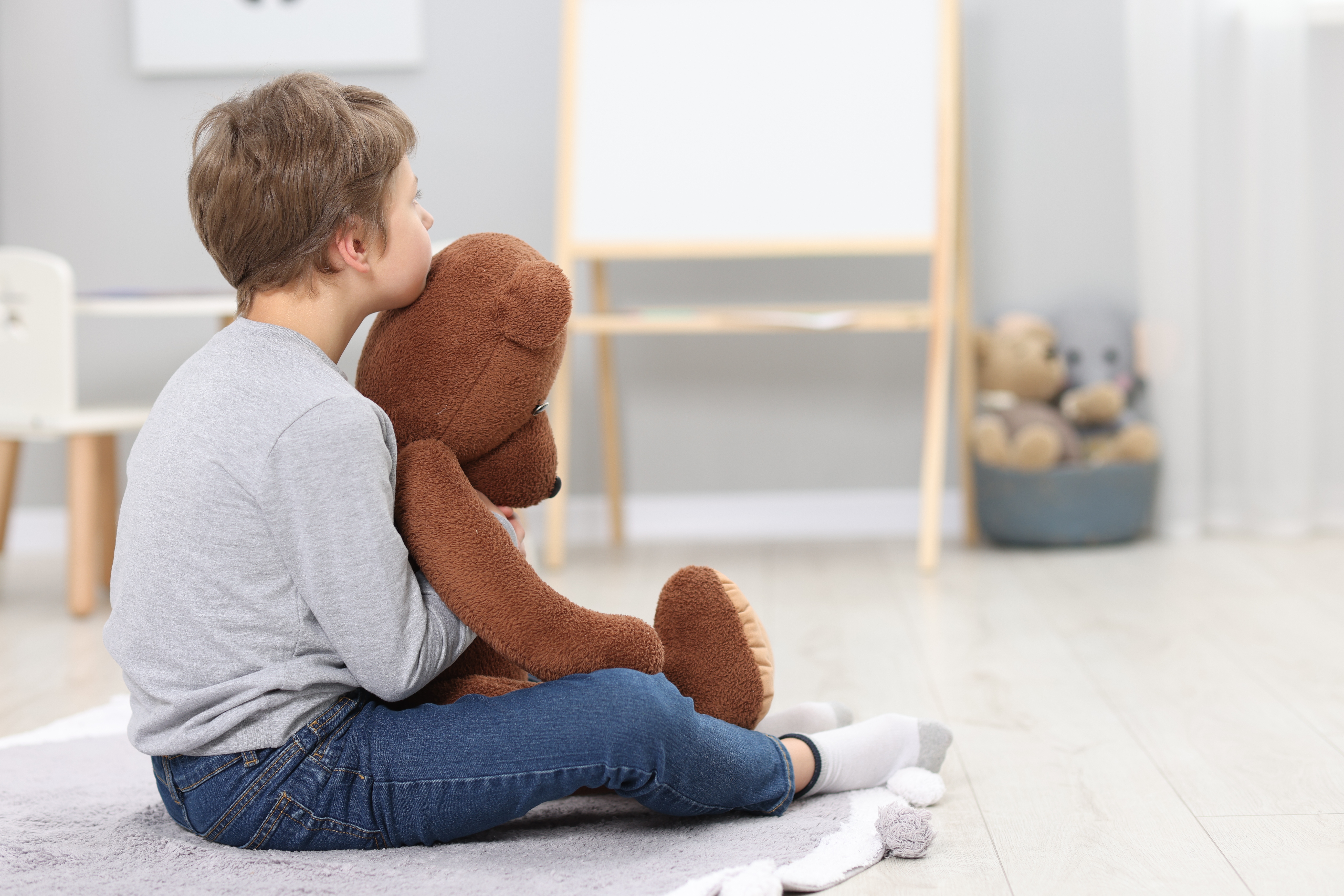Kleiner Junge sitzt allein in seinem Zimmer mit einem großen Teddybär, weil er traurig ist